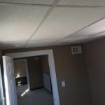 Interior hallway with tan walls, drop ceiling, and doors on the left side.