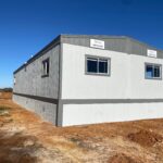 A white and gray building sitting in the middle of a field.