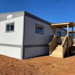 A white and gray container home with stairs leading to the front.